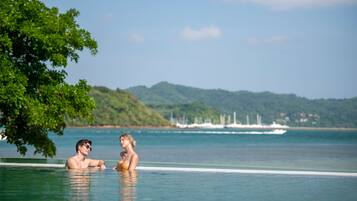 A couple in a clear, calm pool with a view of a distant shoreline and boats.