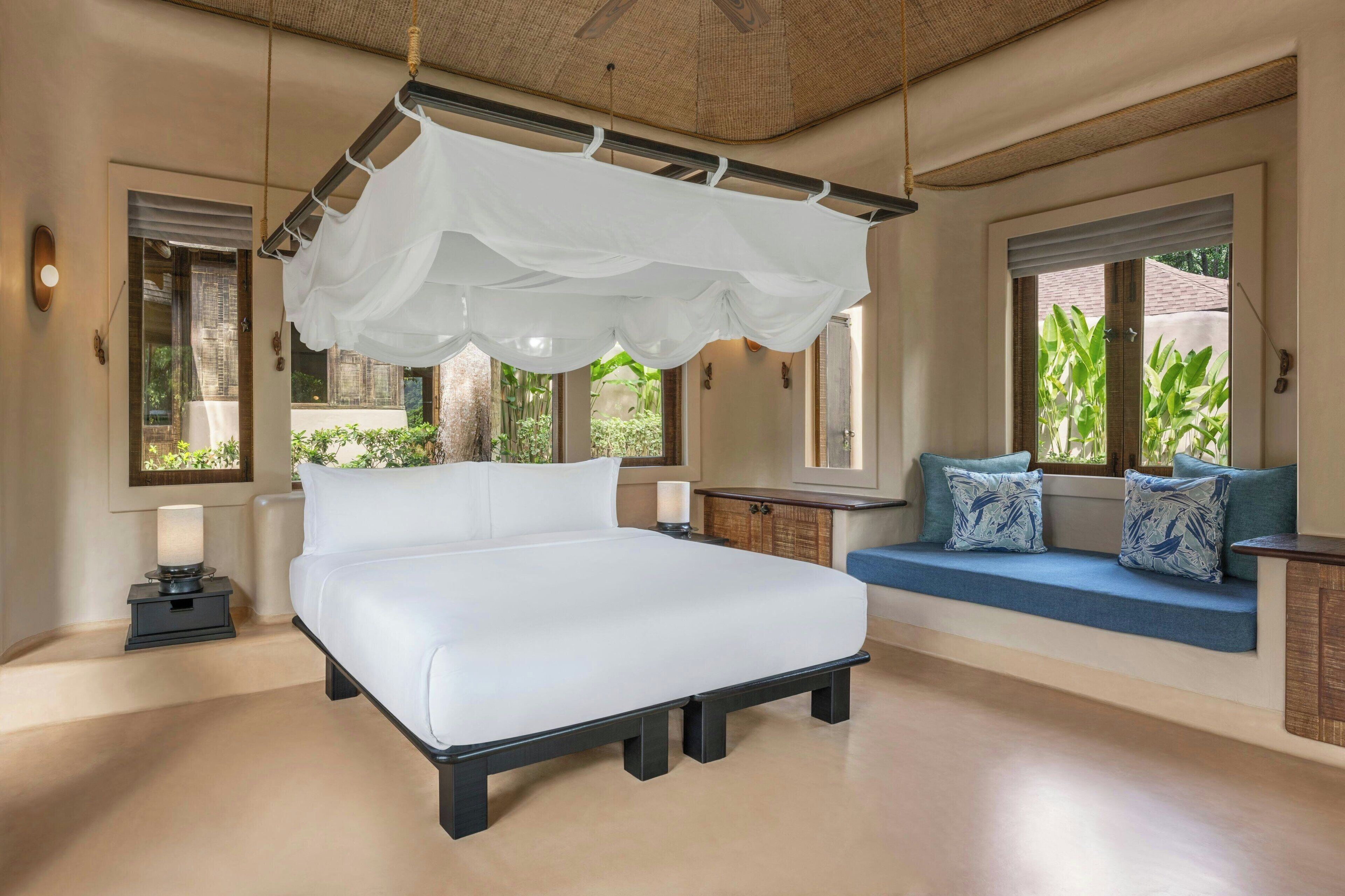 A bedroom with a large bed, a canopy, a sofa with cushions, and a view of greenery outside.