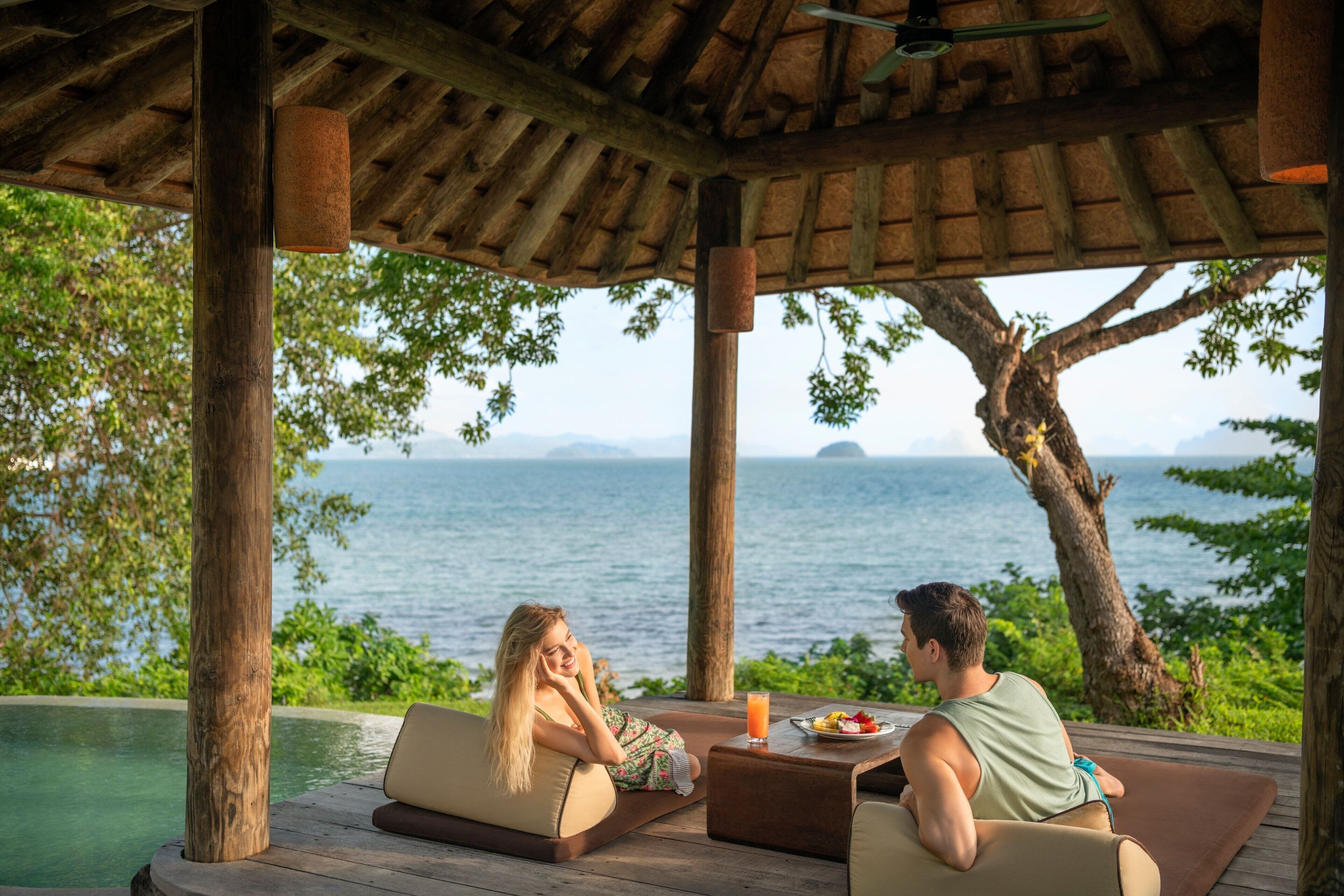 A couple relaxing by a pool with a view of the sea and mountains.
