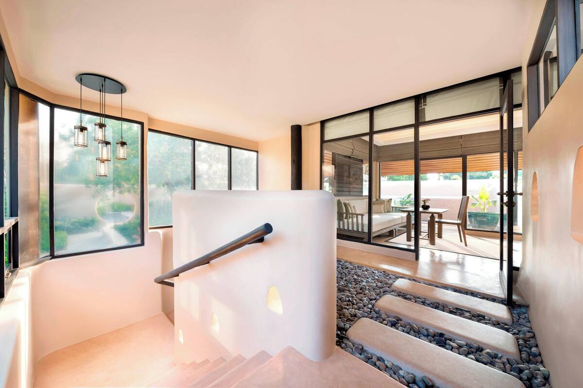 A modern staircase with glass railings, a stone pathway, and a dining area visible through large windows.