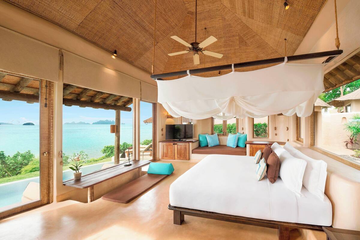 A spacious bedroom with a large bed, a TV, and a view of the sea.