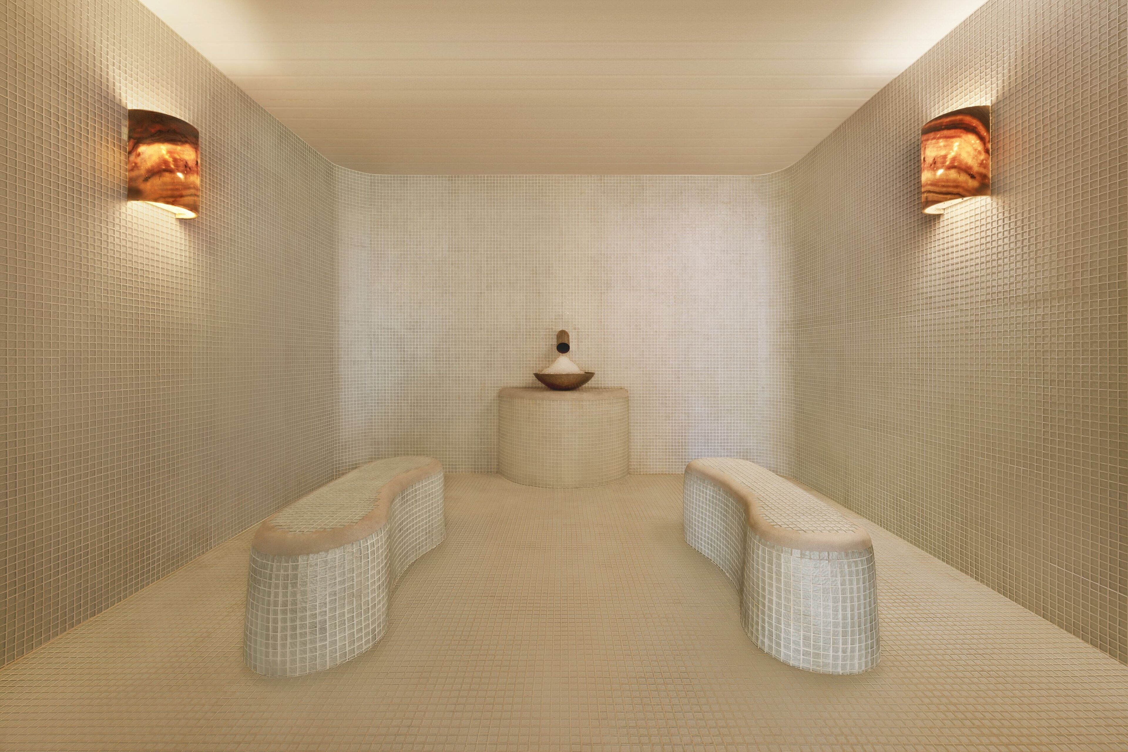 A spa room with a tiled floor, two benches, and a central decorative bowl.