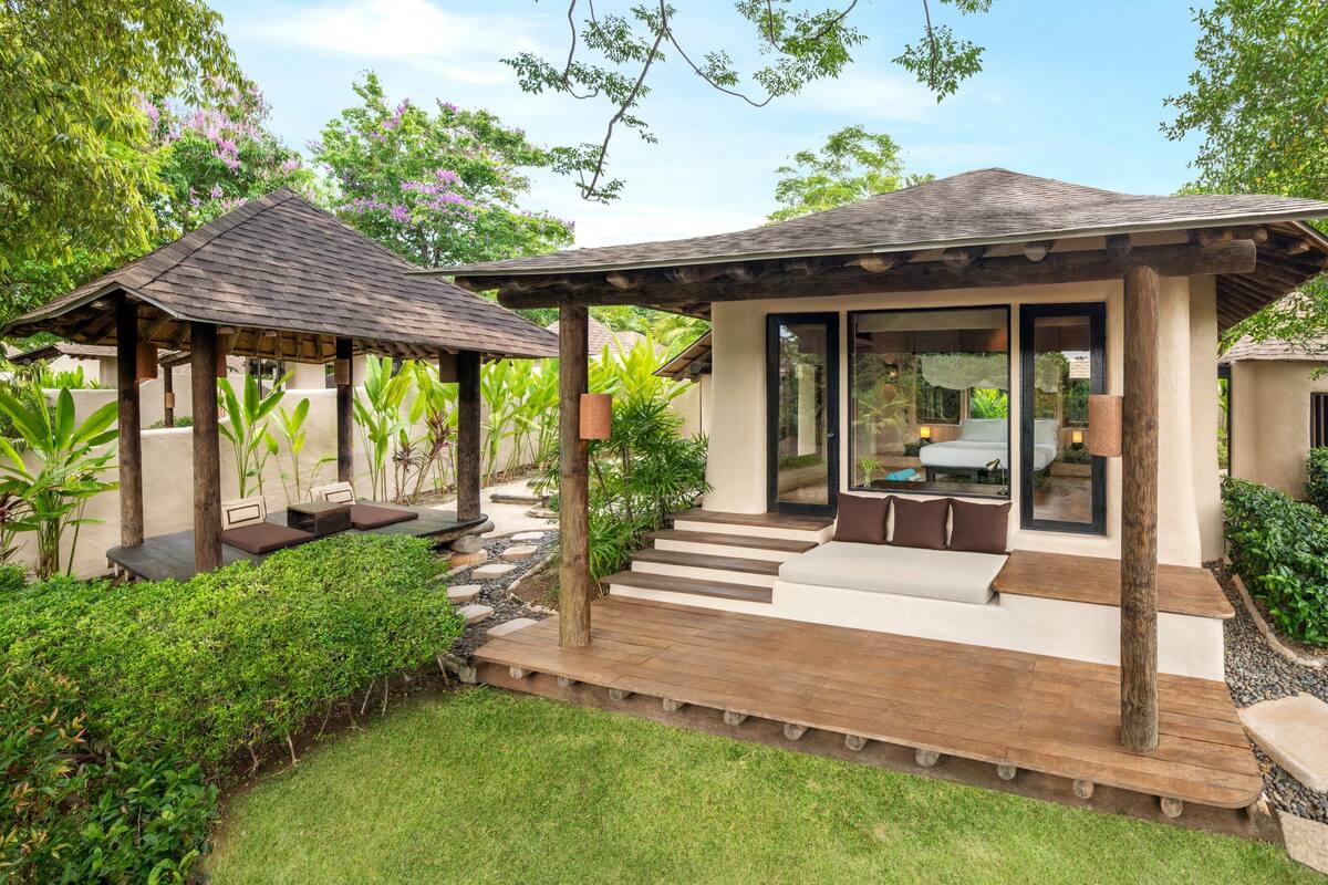 A modern outdoor lounge area with a wooden deck, seating, and a glass-enclosed space.