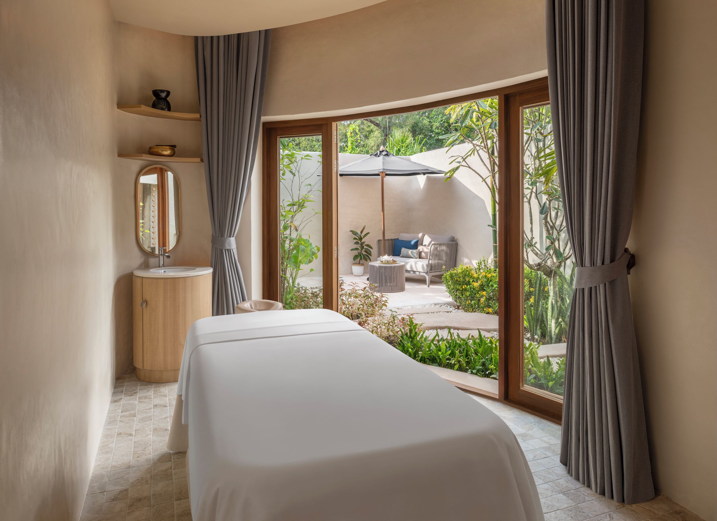 A bedroom with a bed, a vanity, a mirror, and a view of an outdoor patio with a table and chairs.