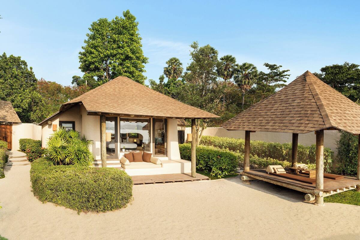 A resort with a covered seating area, a pool, and lush greenery.