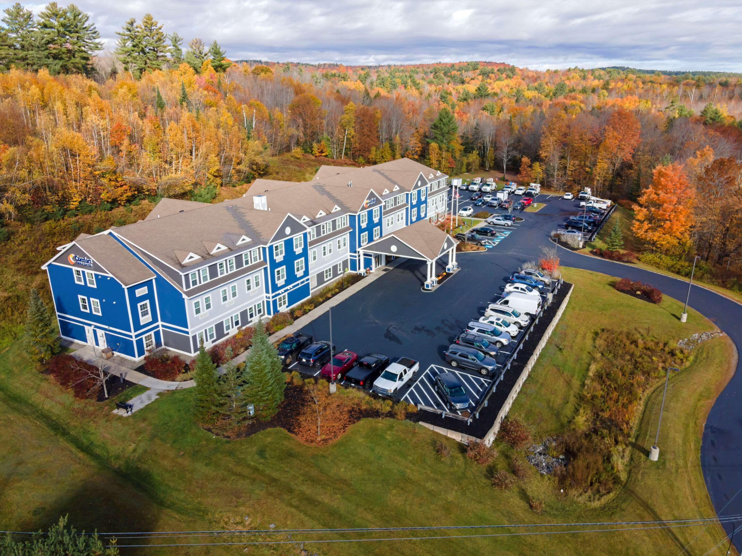 A multi-story hotel with a parking lot and a view of autumn-colored trees.