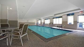 A swimming pool with a tiled deck, white chairs, and a table.