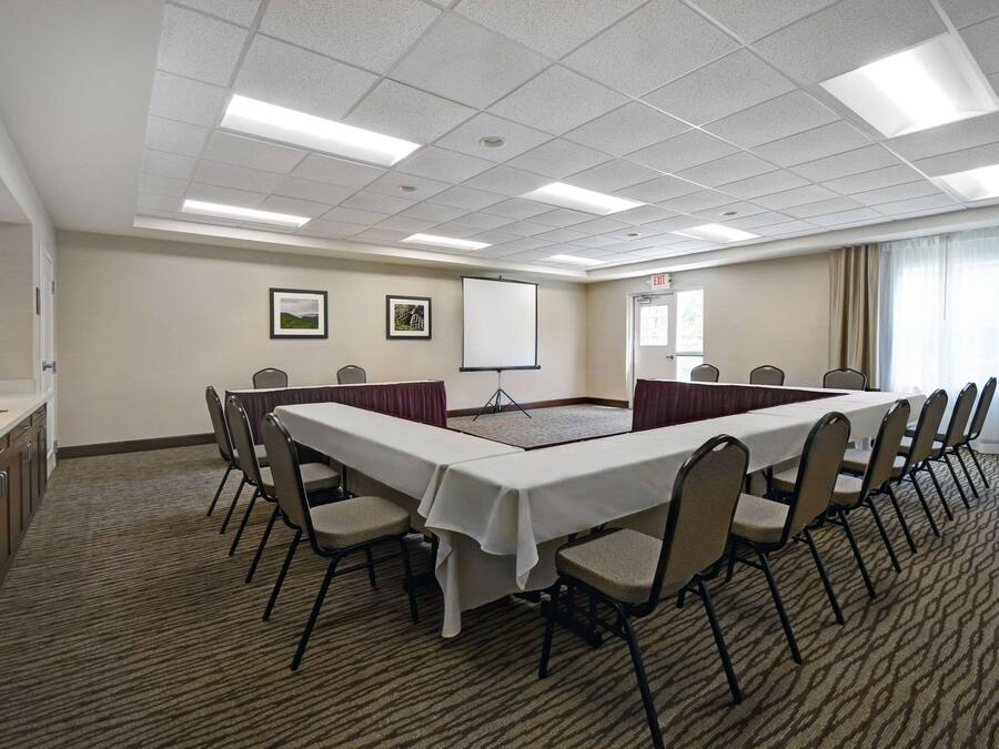 A conference room with a long table, chairs, a projector screen, and a carpeted floor.