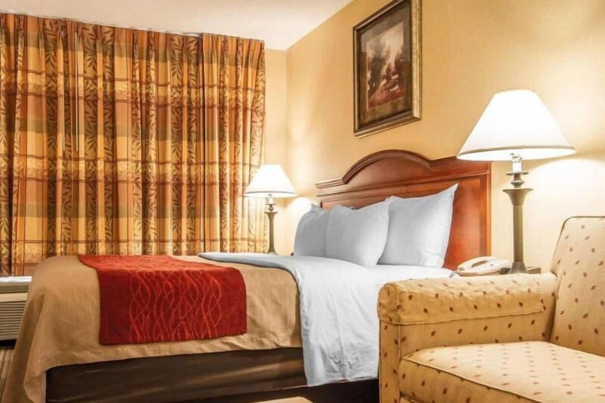 Une chambre d’hôtel avec un lit, deux lampes de chevet, une chaise, une table et un tableau au mur.