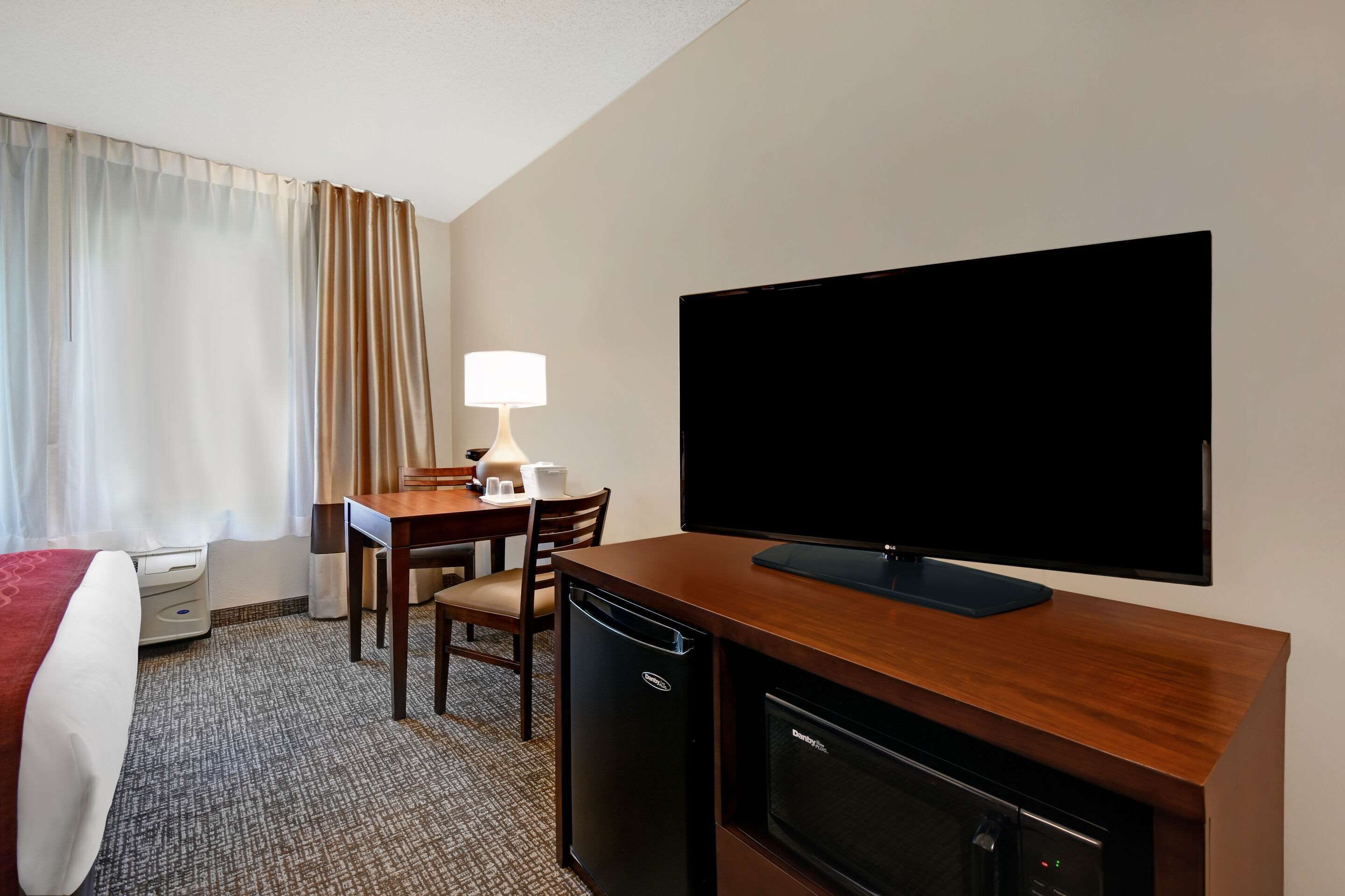 Una habitación de hotel con una cama, un escritorio con lámpara, televisión y un refrigerador pequeño.