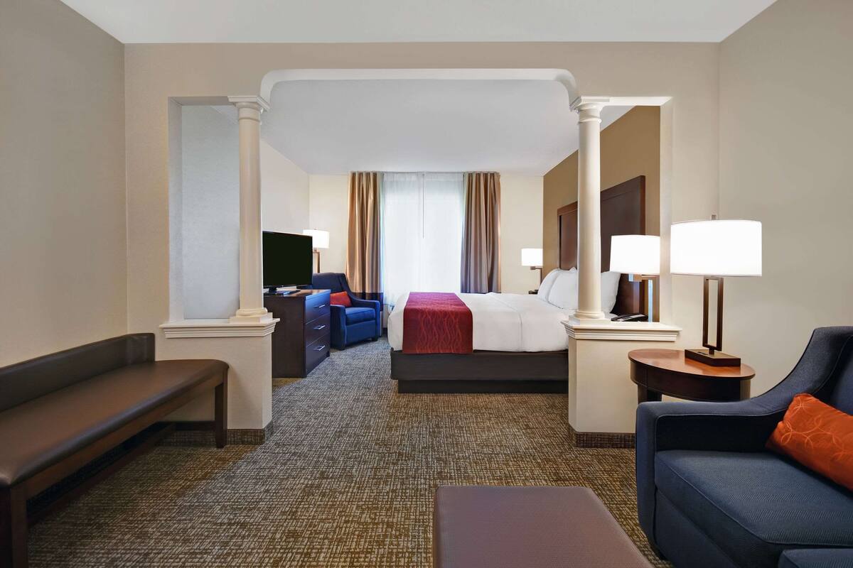 Une chambre d’hôtel avec un grand lit, un canapé, une banquette et un bureau avec une lampe.