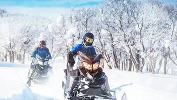 Dos motos de nieve en un sendero cubierto de nieve, con árboles al fondo.