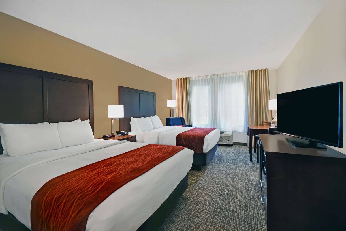 Une chambre d’hôtel avec deux lits, un bureau, une télévision et une fenêtre avec des rideaux.