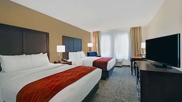 Habitación de hotel con dos camas, un escritorio, un televisor y una ventana con cortinas.