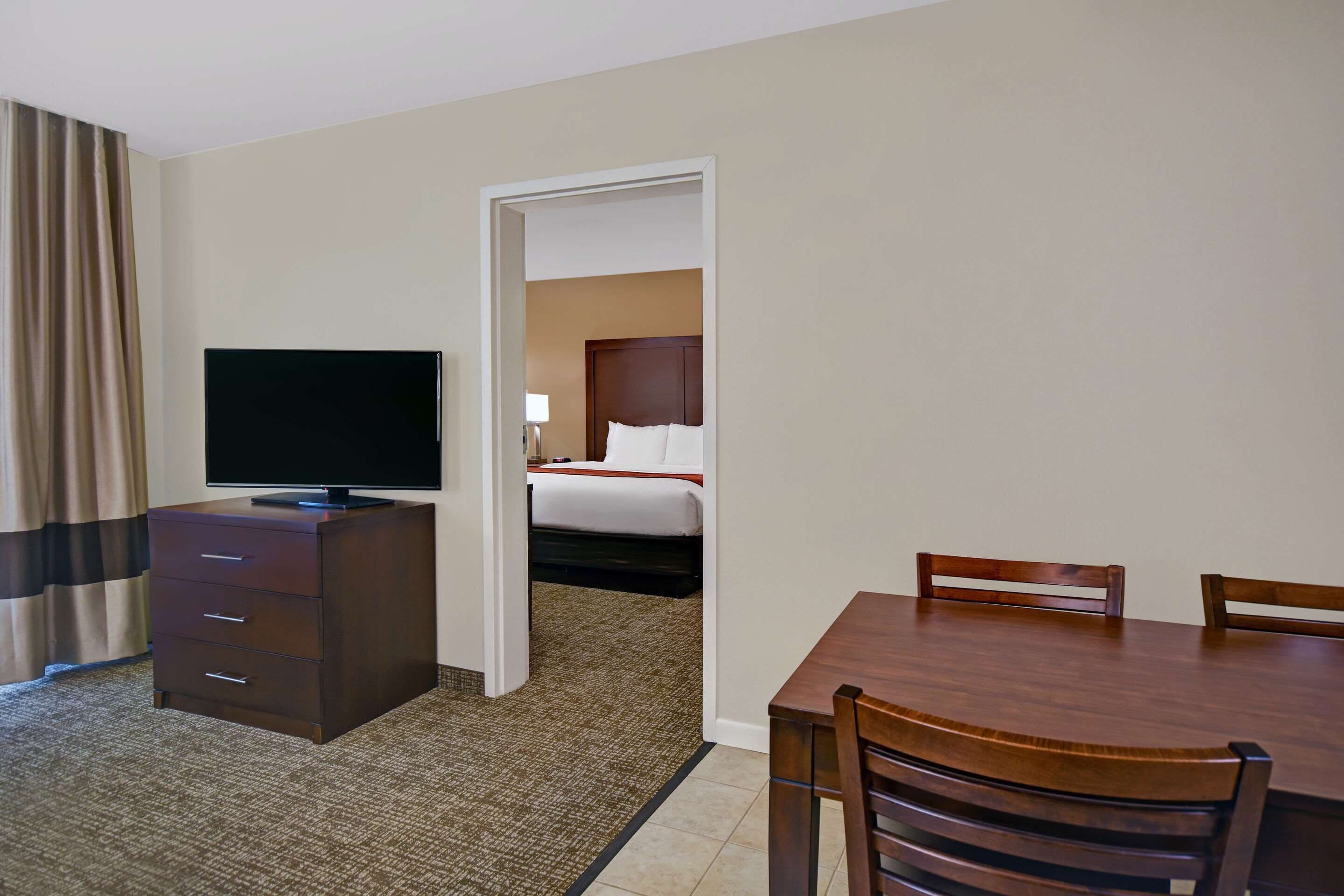 A hotel room with a TV on a dresser, a bed with a white comforter, and a dining table with chairs.