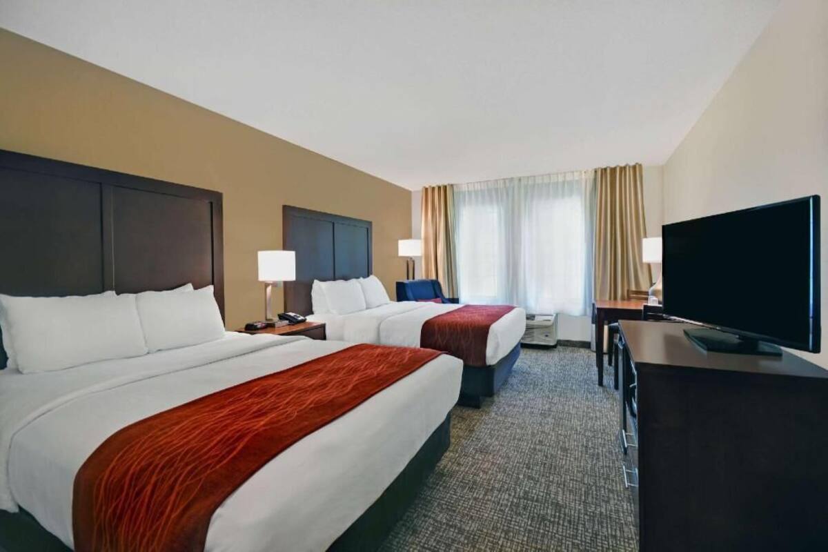 Une chambre d’hôtel avec deux lits, un bureau, une télévision et une fenêtre avec des rideaux.
