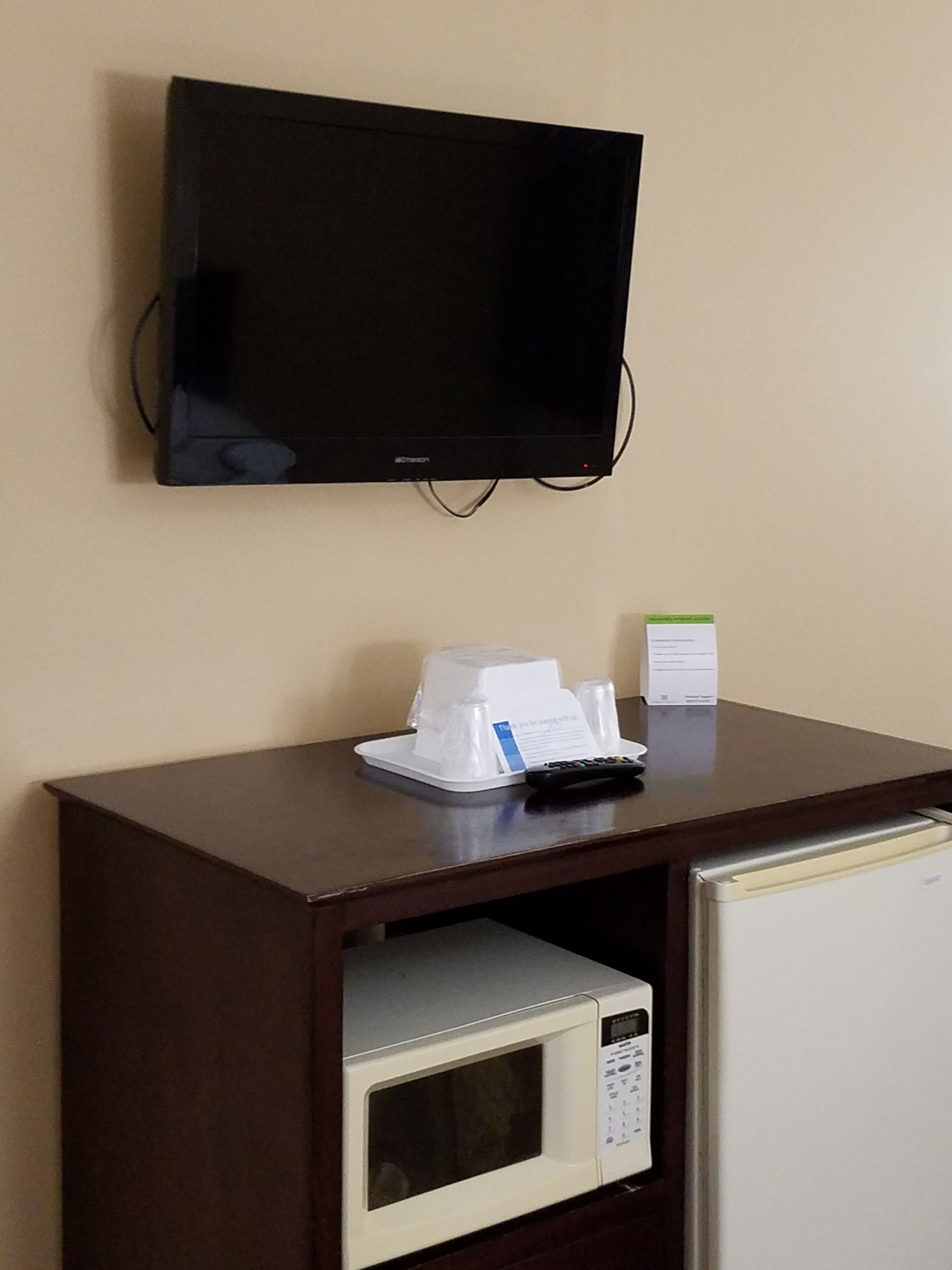 A small kitchenette with a microwave, a coffee maker, and a television mounted on the wall.