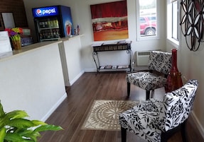 Un vestíbulo con mostrador de recepción, refrigerador de Pepsi, un cuadro, alfombra estampada y una silla con tapicería floral.