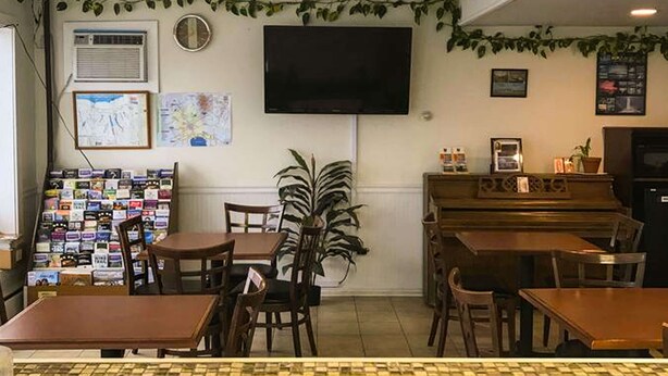 A cozy cafe with a flat-screen TV, a piano, and a variety of seating options including tables and chairs. - Rodeway Inn Manchester I-90 (Manchester)