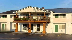 A two-story building with a balcony, a parking lot, and a green door. - Rodeway Inn Manchester I-90 (Manchester)