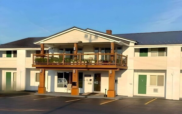 A two-story building with a balcony, a parking lot, and a green door.
