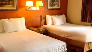 A hotel room with two beds, a nightstand, and wall-mounted lamps. - Rodeway Inn Manchester I-90 (Manchester)