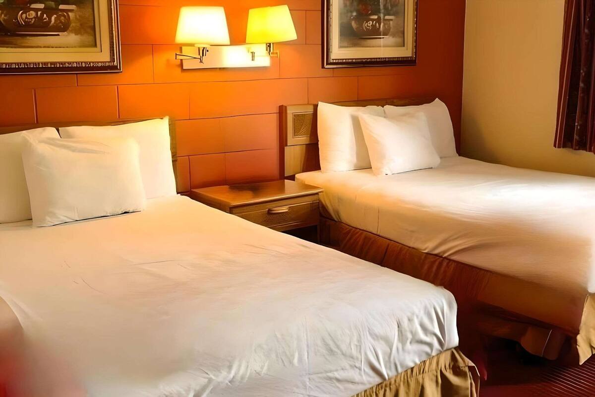 Hotellihuone, jossa on kaksi sänkyä, yöpöytä ja seinään kiinnitetyt lamput.