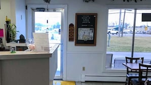 A reception area with a counter, a framed notice board, and a view of the outside through a glass door. - Rodeway Inn Manchester I-90 (Manchester)