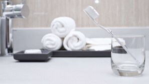 A bathroom with a glass of water, a toothbrush, and rolled towels.