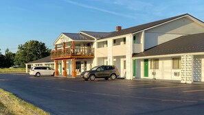 A motel with a two-story structure, a balcony on the first floor, and a parking lot with two cars.