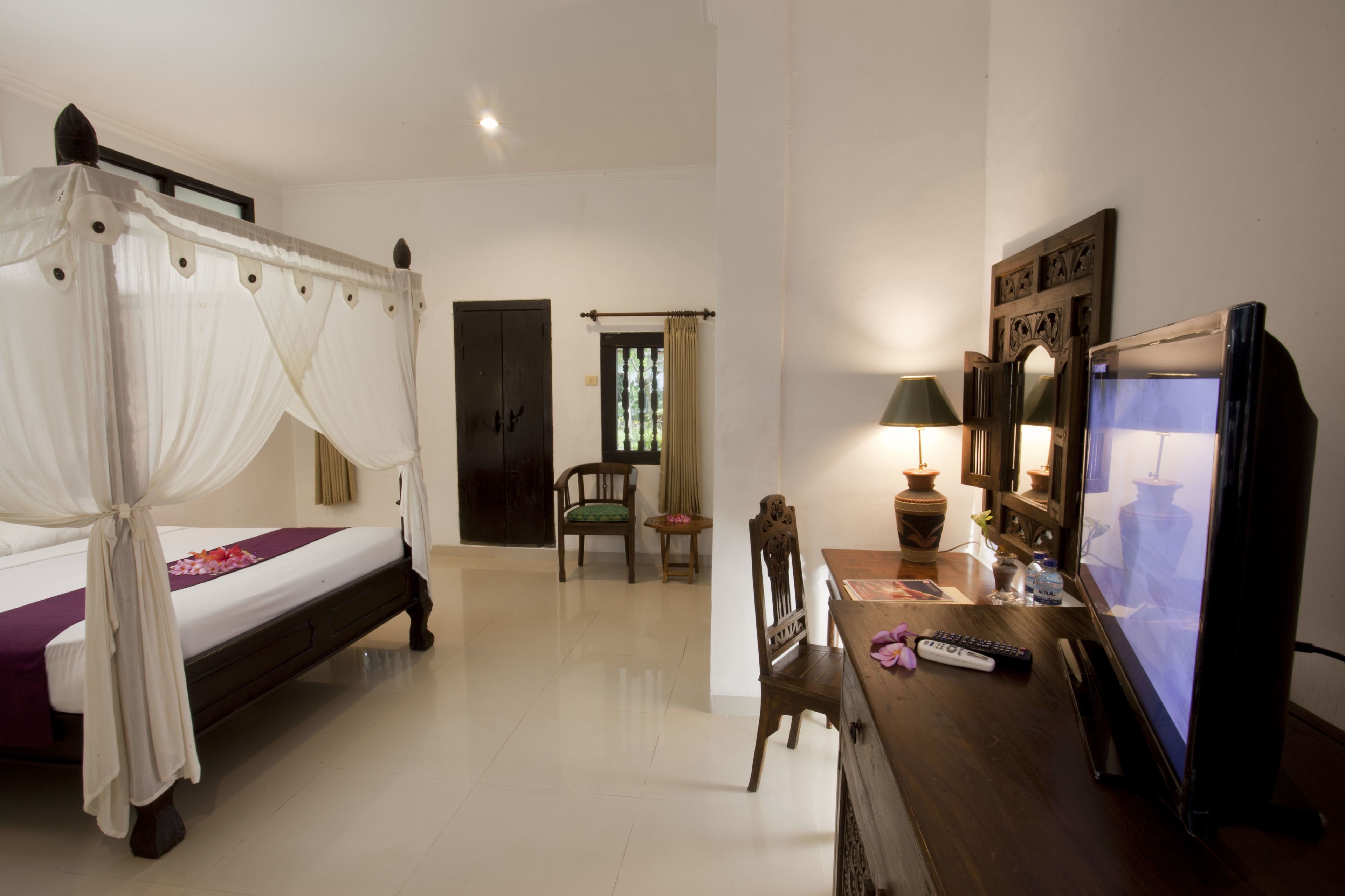 Quarto com cama de dossel, escrivaninha de madeira com televisão e uma cadeira.