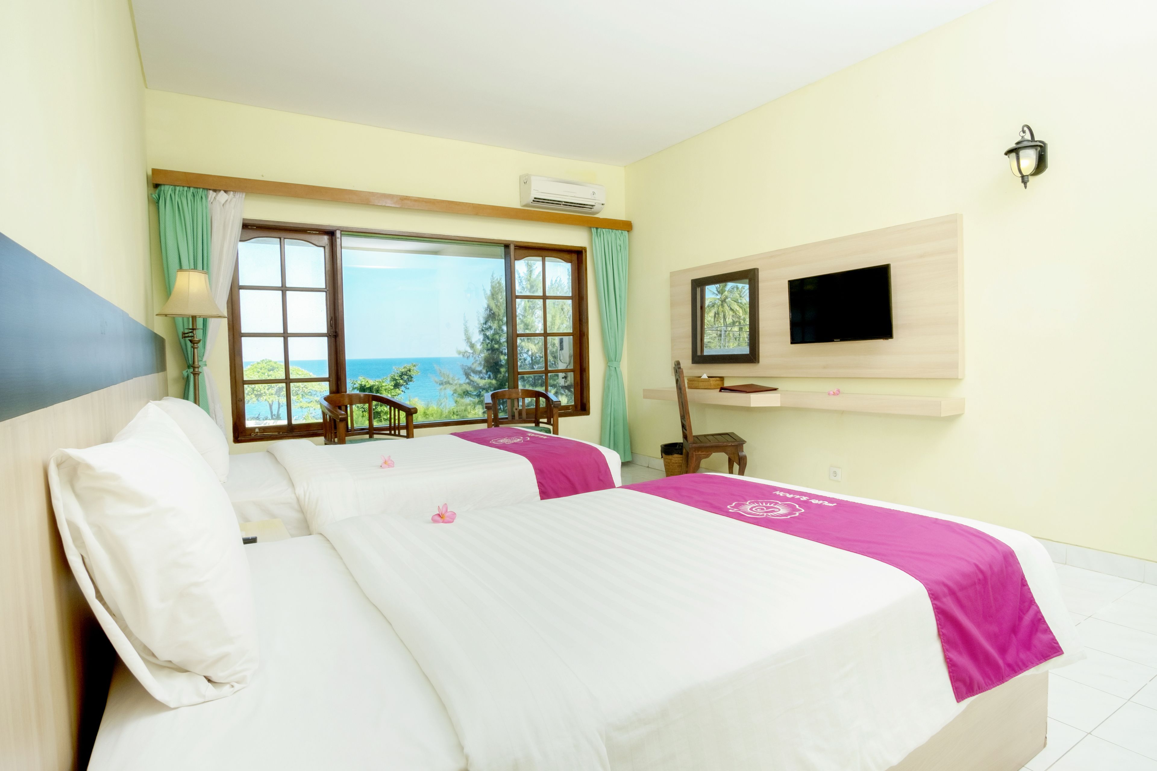A hotel room with two beds, a TV, a window with a view of the sea, and a chair by the window.