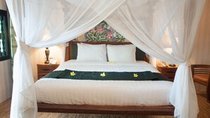 Een bed met hemelbed, nachtkastje met een lamp en een bloemen behang.