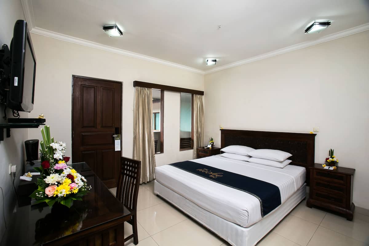 Habitación de hotel con una cama grande, un escritorio con silla, un televisor y un arreglo floral.