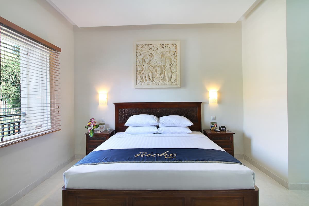 Una cama bien hecha con un cabecero decorativo, dos mesitas de noche con lámparas y una obra de arte en la pared.