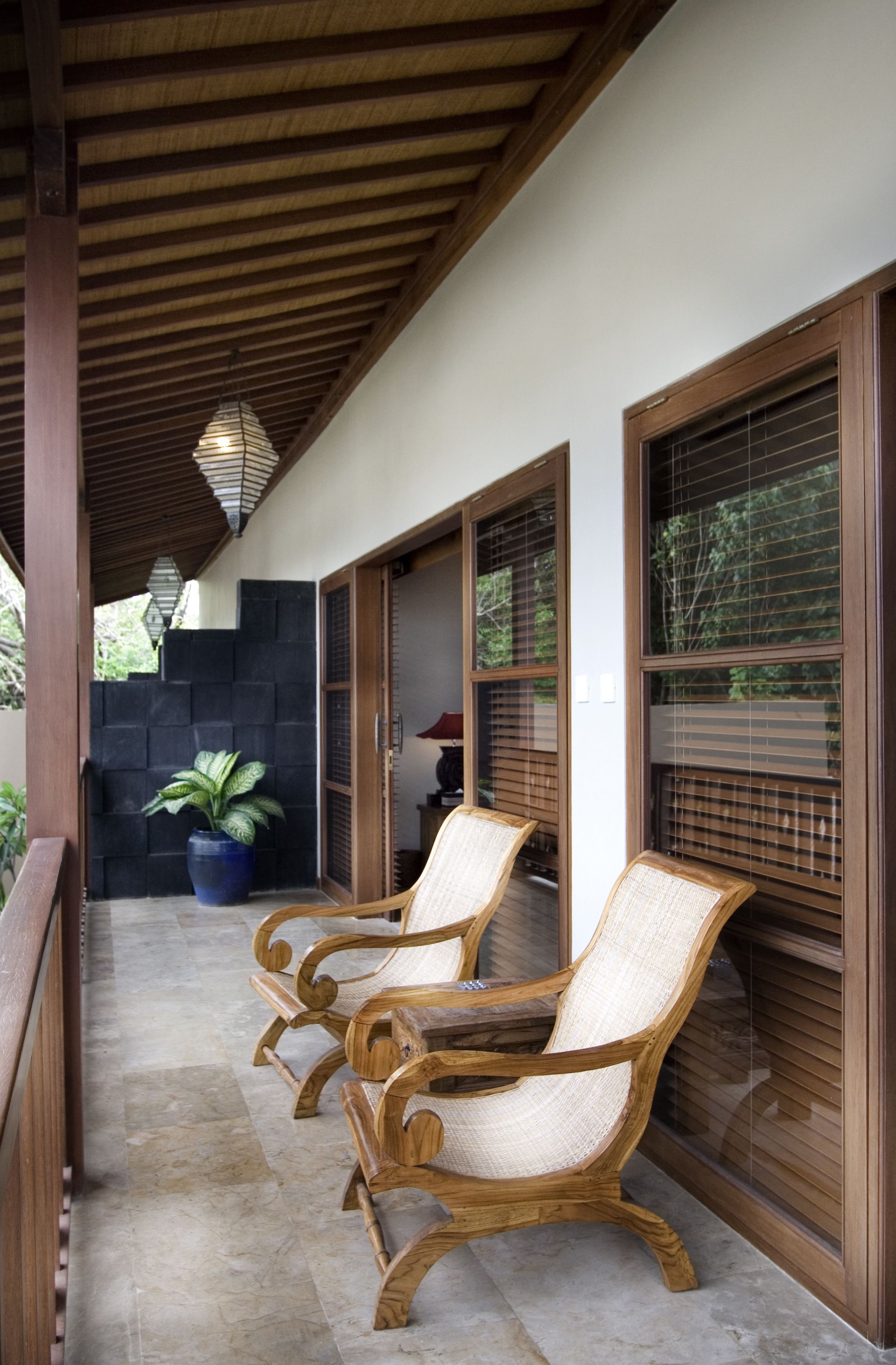 Un espace extérieur abrité, aménagé avec des chaises en bois et un pot de fleurs.