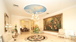 A spacious lobby with a central glass table, elegant chairs, a chandelier, and a large floral painting on the wall. - Gran Hotel Diligencias (Veracruz)