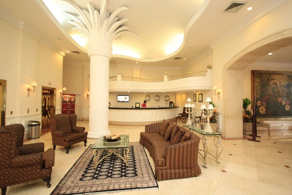 A spacious lobby with a high ceiling, a reception desk, seating area with sofas and armchairs, and a large decorative column. - Gran Hotel Diligencias (Veracruz)