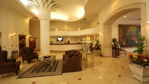 A spacious lobby with a high ceiling, a reception desk, comfortable seating, and a large painting. - Gran Hotel Diligencias (Veracruz)