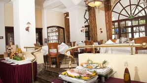 A hotel lobby with a marble staircase, wooden chairs, a buffet table with fruits and seafood, and a chandelier. - Gran Hotel Diligencias (Veracruz)
