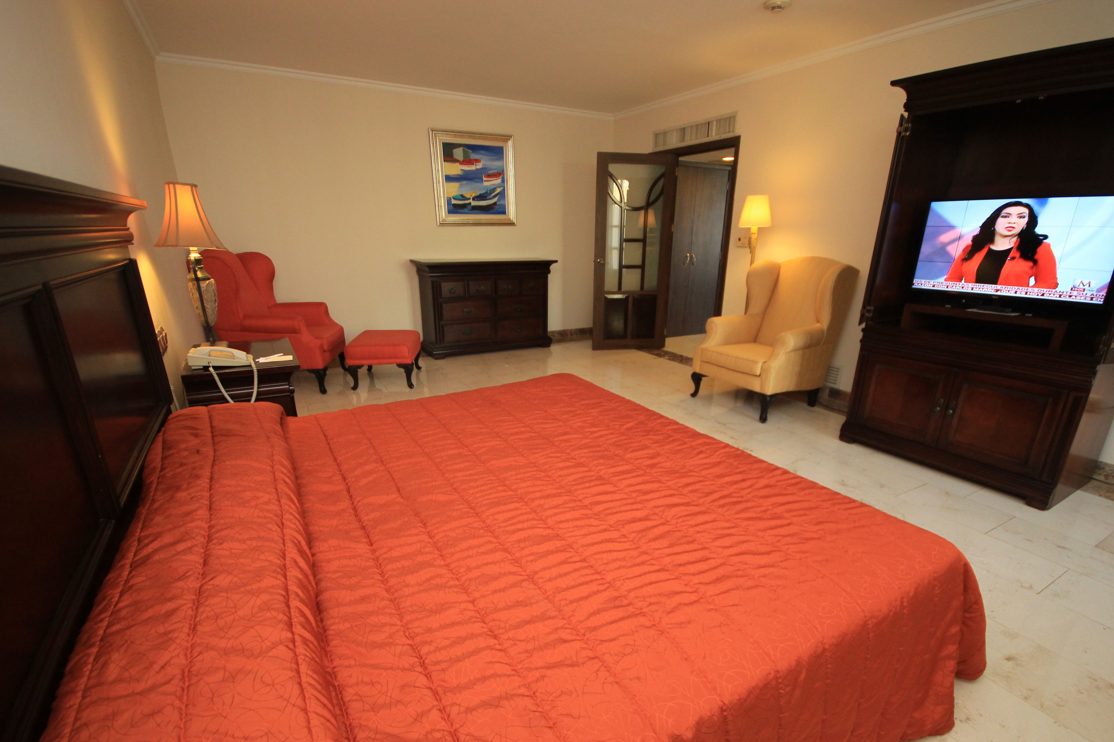 A hotel room with a large bed, a TV, a fireplace, and a painting on the wall.