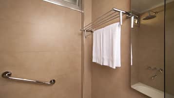 Un baño moderno con una cabina de ducha de vidrio, una toalla blanca colgada en un perchero y una barra de apoyo.
