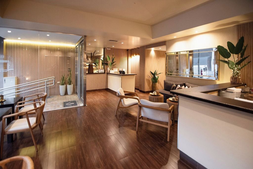 A modern hotel lobby with a reception desk, seating area, and a large mirror reflecting the interior.