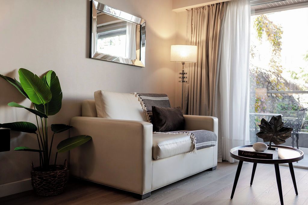 Una sala de estar moderna con sofá, lámpara, planta en maceta y una mesa con un objeto decorativo.