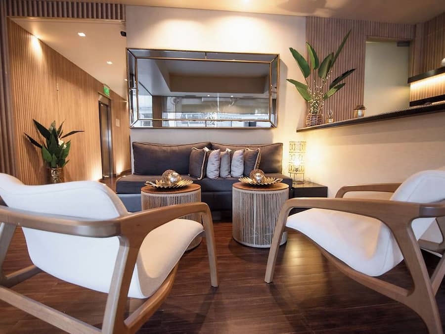 Una sala de estar moderna con un sofá, dos sillones, una mesa de centro y una mesita auxiliar. Hay un espejo grande sobre el sofá y una planta en maceta al lado.