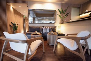 Un salon moderne avec un canapé, deux fauteuils, une table basse et une table d’appoint. Un grand miroir est placé au-dessus du canapé, et une plante en pot se trouve sur la table d’appoint.