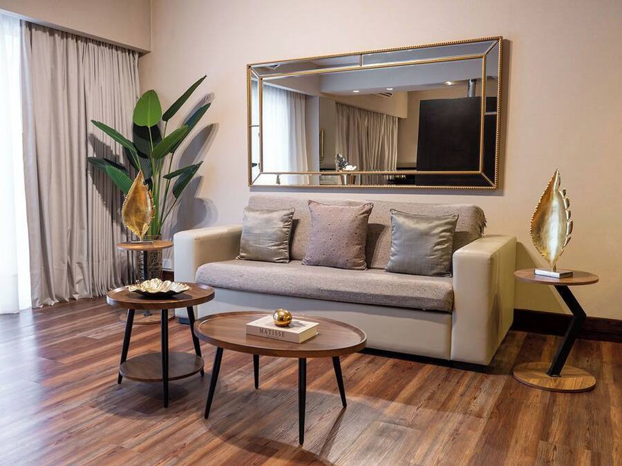 A modern living room with a sofa, two coffee tables, a large mirror, and a potted plant.