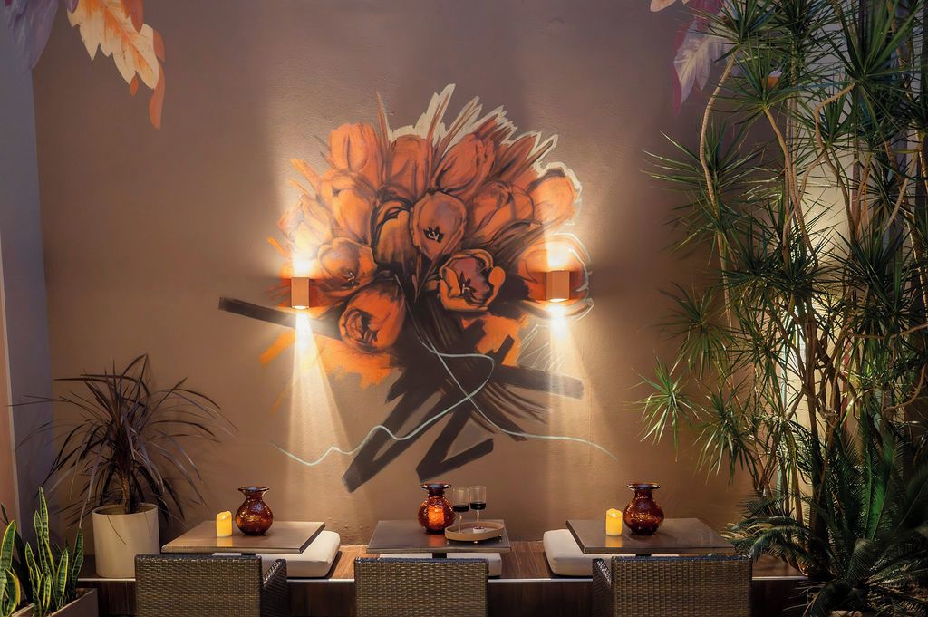 A restaurant interior with a mural, tables, chairs, and potted plants.