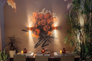 L’intérieur d’un restaurant, avec une fresque murale, des tables, des chaises et des plantes en pot.