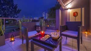 Ein Balkon mit Korbstühlen, einem Tisch, einem Weinglas, Snacks und Laternen.